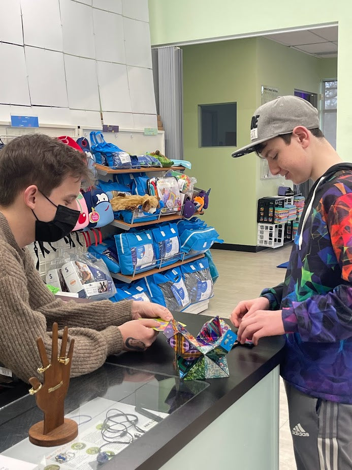 Man helps a teenager at a counter demonstrating a product
