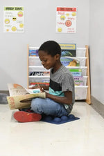 A child sits cross legged on the SitSmart on the floor. They are reading a book in their lap.