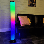 The PlayLearn 3.3 ft Color-Changing Sensory LED Light Up Tower next to a couch in a dimly lit room.