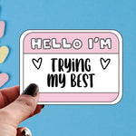 A hand holds the pink Hello I'm Trying My Best 3" sticker.