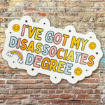 The rainbow colored I've Got My Disassociates Degree Vinyl Sticker on a brick background.