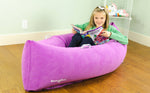 A child smiling and holding an open workbook. They are sitting in a purple Hugging Peapod (60").