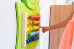 A child with medium skin tone points to the multicolored beads of the abacus on the Frog Activity Wall Panel.