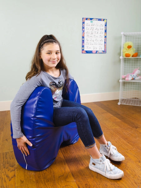 A child with light skin tone and a long brown ponytail sits on the Sensory Soft Squeeze Seat by Bouncyband.