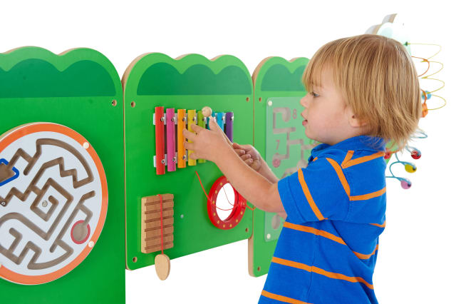 A child with light skin tone and short blonde hair plays with the xylophone on the Crocodile Activity Wall Panels.