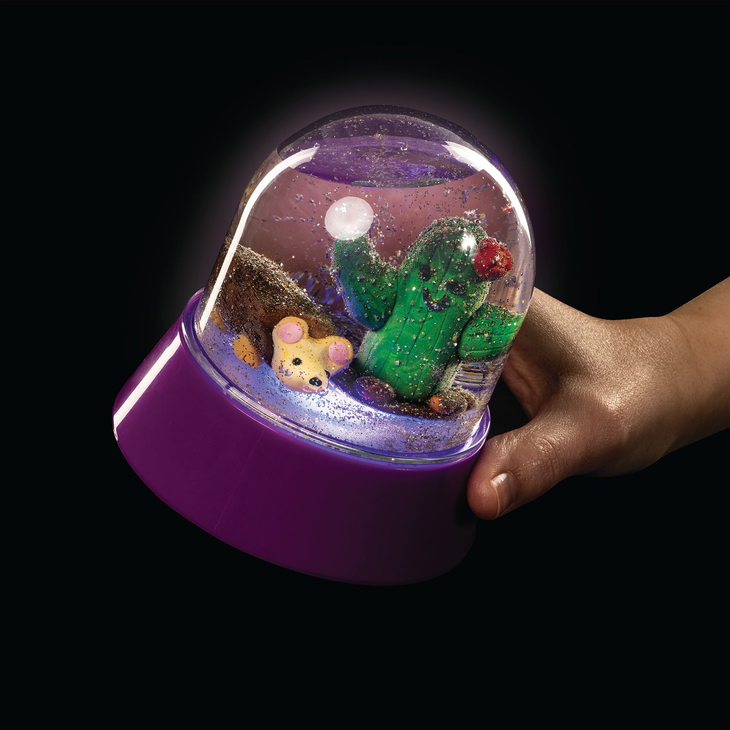 A hand with medium skin tone holds up an illuminated MYO Light Up Snow Globe.