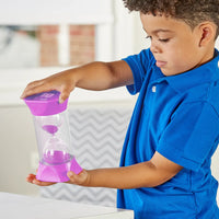 A child with medium skin tone and short curly dark brown hair is holding the Jumbo 10 Minute Sand Timer between both of their hands. They are watching the sand fall from the top chamber to the bottom.