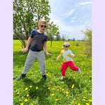 One small and one tall child stand in a green field full of yellow dandelions in the two versions of the Easy to See Sensory Friendly T-Shirt.