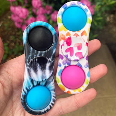 A hand holds two of the 2 Sided OMG Mega Pop Fidget Spinners.