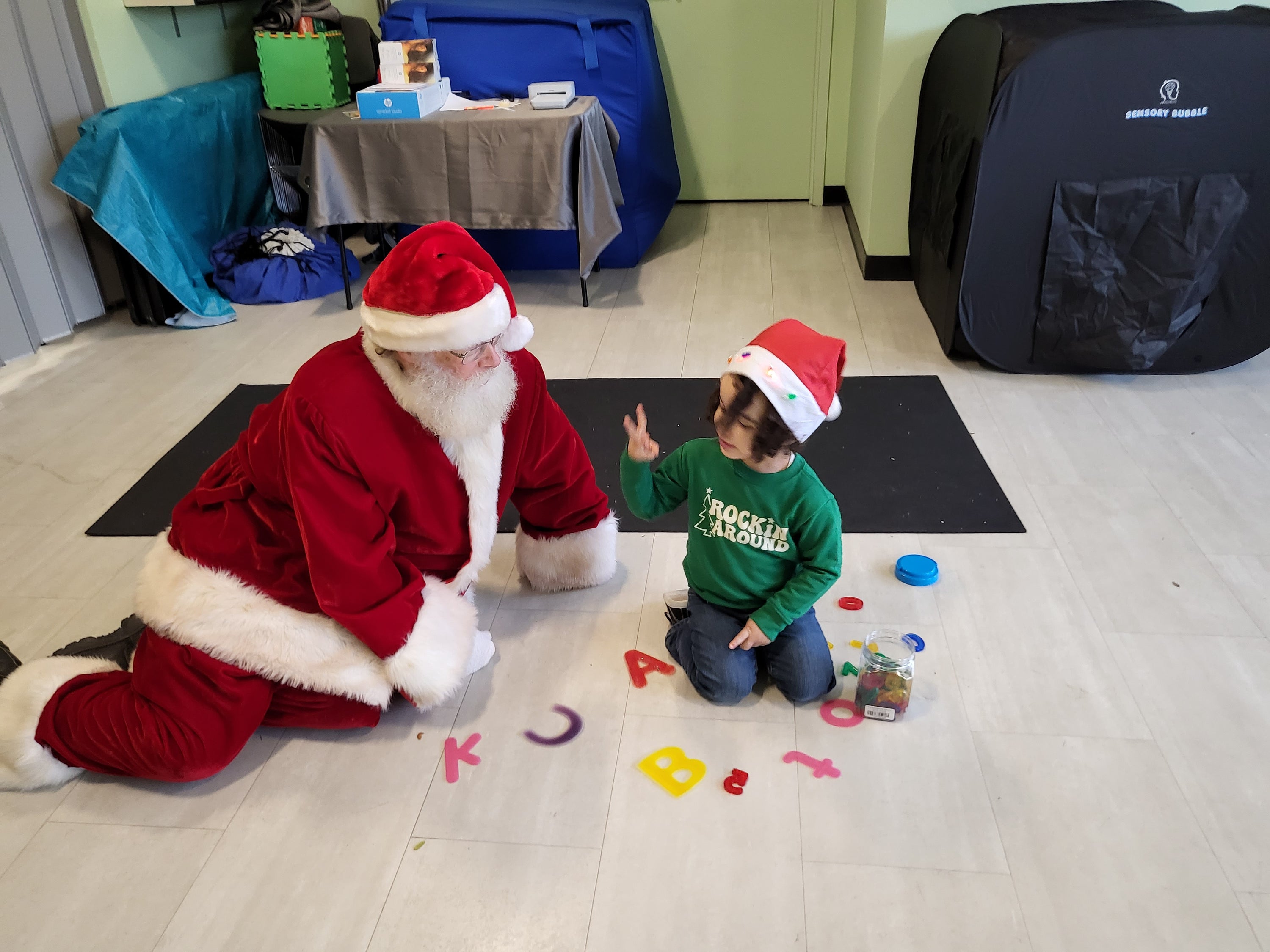 Child sits on the floor with Santa playing with letters
