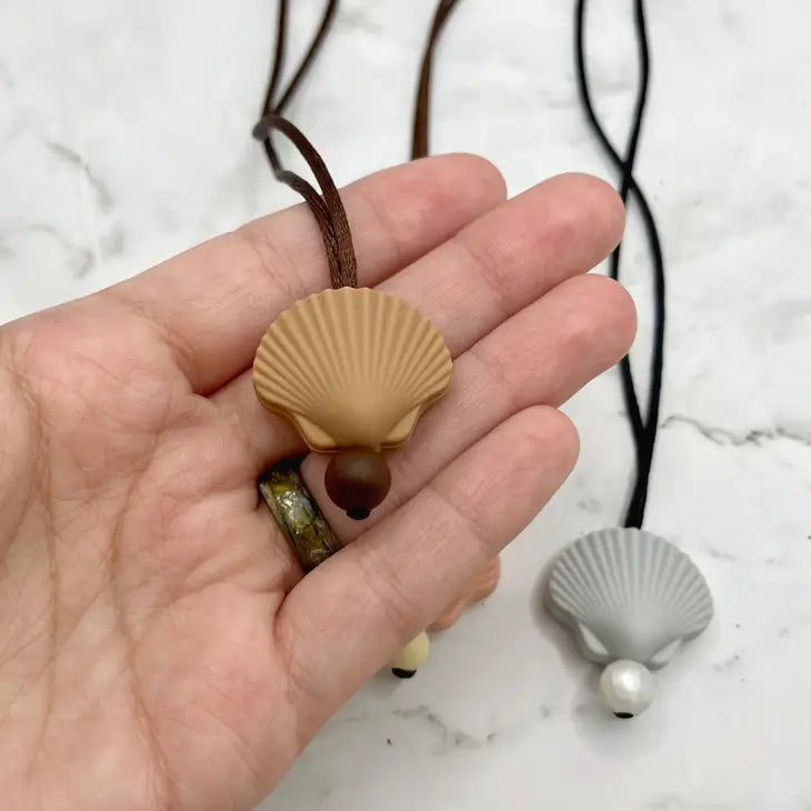 A hand holds up the Shell Chewy Fidget Necklace.