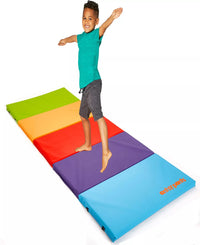 A child with medium skin tone and short brown hair stretches their arms and leg out on top of the vibrant Antsy Pants Tumbling Mat.