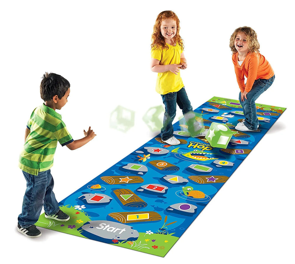 Two children are posed on the vinyl board at the end of the "creek." One child is standing at the other end, where the "Start" spot is on the board. They are throwing the giant dice to see where to move.