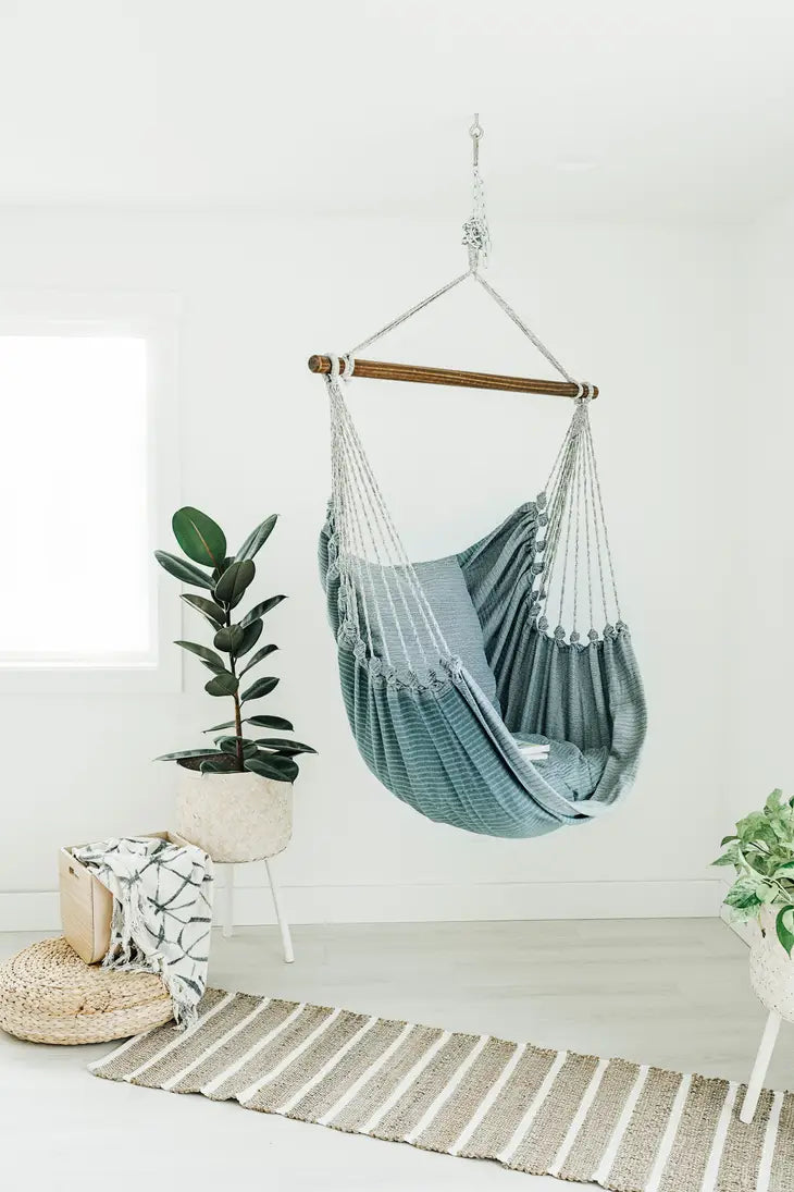 The Denim Hanging Chair displayed in a white room with a potted plant and a rug.
