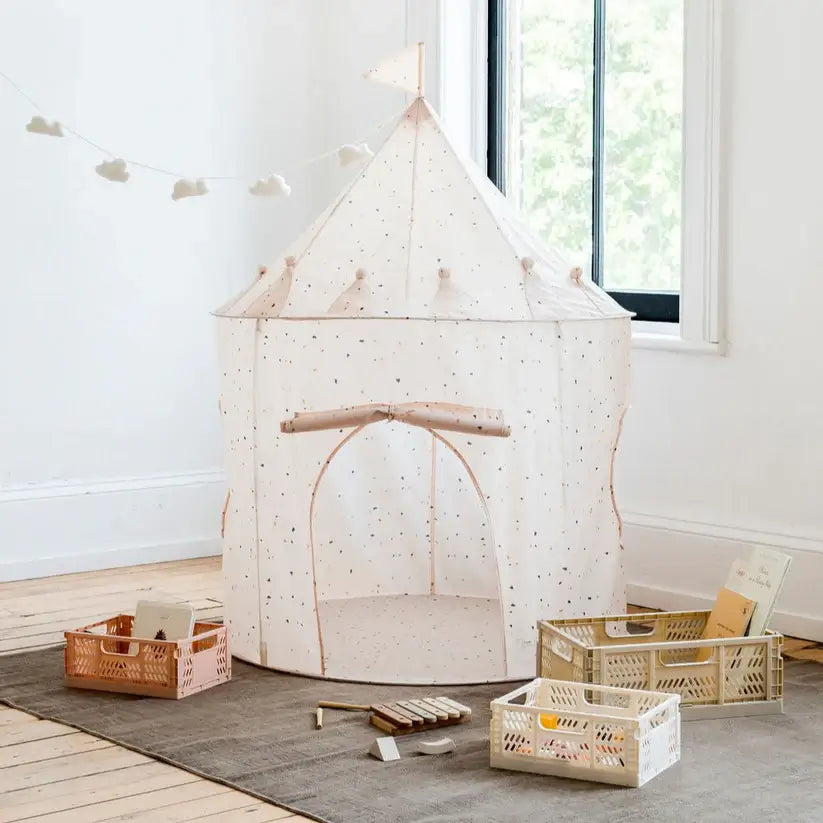 The terrazzo beige Play Tent Castle is sitting on a brown rug next to several containers full of toys and a xylophone.