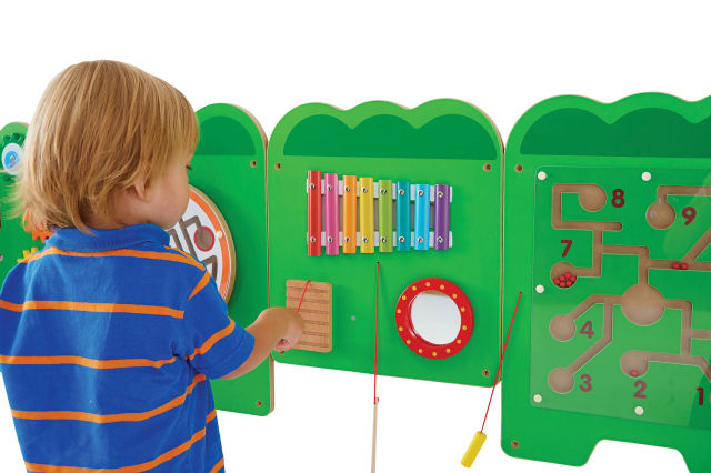 A child with light skin tone and short blonde hair plays on the wooden percussive instrument on the Crocodile Activity Wall Panels.