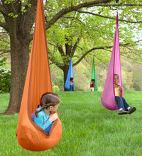 Several children are suspended from trees in brightly colored HugglePod Lite Nylon Hanging Chairs.