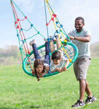Two children are belly down on the 2-in-1 Climbing Rope Swing. An adult smiles while pushing the swing.