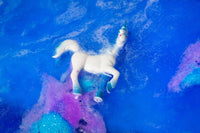 A toy unicorn is half submerged in blue and purple fizz.
