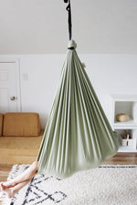 A child leans back in the Desert Sage Sensory Swing with their legs sticking out of the end.