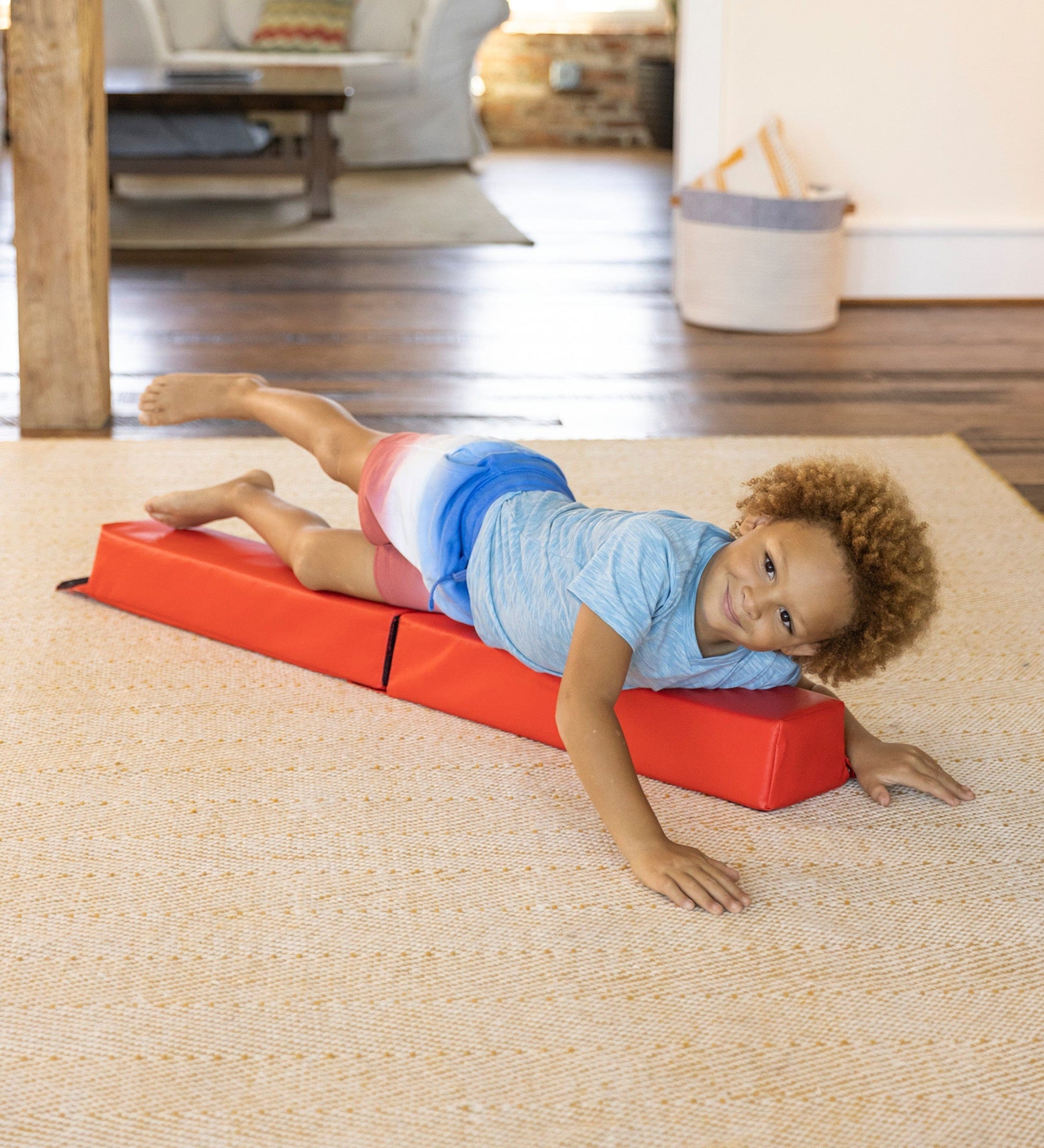 A child with medium skin tone and short brown hair is lying on the 4' Gymnastics Balance Beam, favoring their left side.