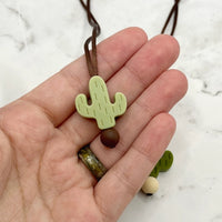 A hand with light skin tone holds up the light green Cactus Fidget Necklace.