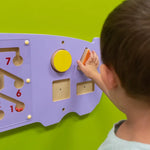 A close up look at a child with light skin tone and short brown hair playing with the shapes on the Hippo Activity Wall Panel.