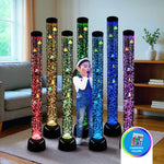 Multiple bubble tubes illuminate a rainbow color behind a child holding her hands up to her face in a living room.