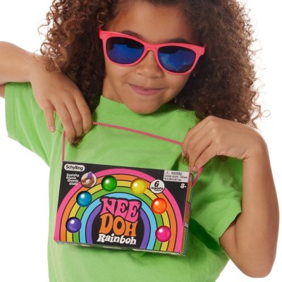  A child with medium skin tone and long curly brown hair is wearing sunglasses. They are holding up the product package for Rainbow Teenie Nee Doh.