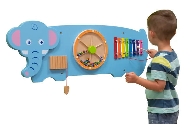 A child with light skin tone and short brown hair plays with the xylophone on the Elephant Activity Wall Panel.