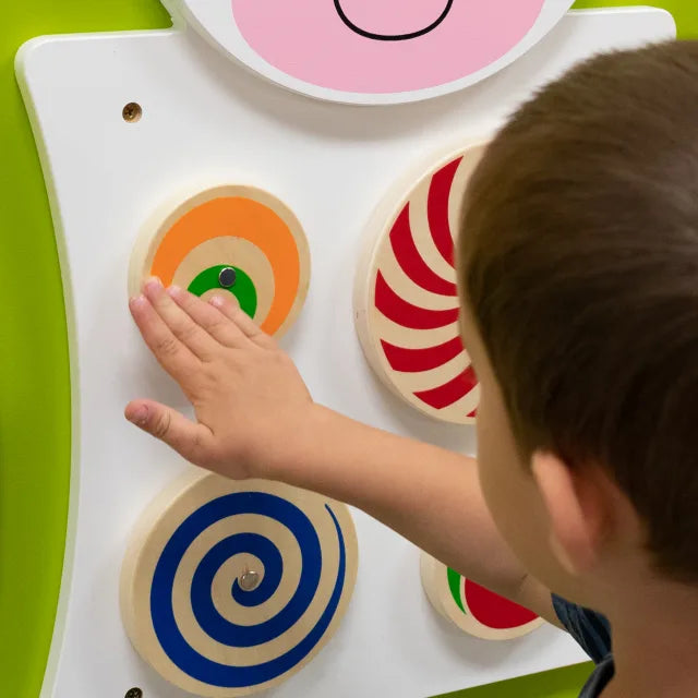 A child with light skin tone and short brown hair spins one of the wheels on the Cow Activity Wall Panel.