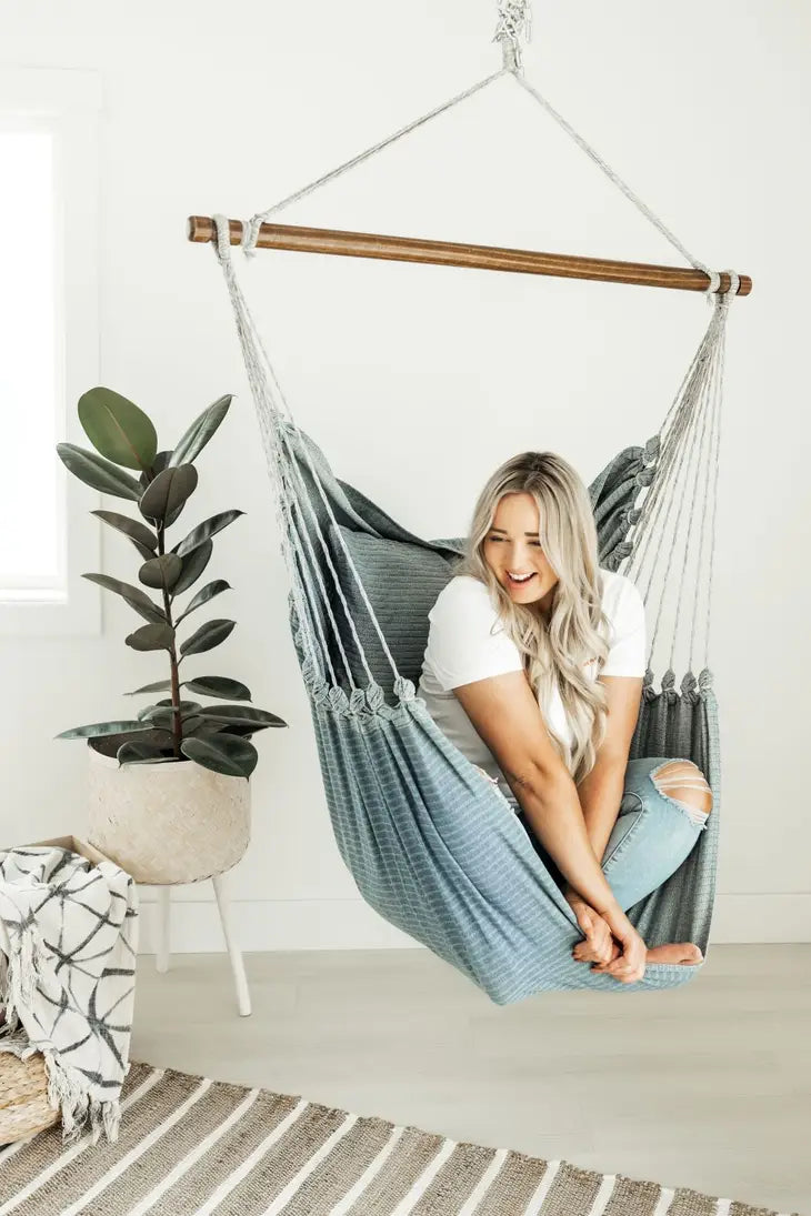 Someone with light skin tone sits cross legged in the Denim Hanging Chair.