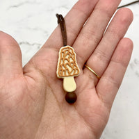 A hand with light skin tone holds up the Morel Mushroom Fidget Necklace.