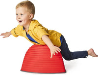 A child with light skin tone and short blonde hair balances on their belly on the tall red Gonge Hilltop.