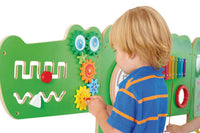 A child with light skin tone and short blonde hair plays with the cogs on the head of the Crocodile Activity Wall Panels.