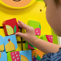 A close-up look of a child with light skin tone moving a tile on the Giraffe Mosaic Fruits Wall Toy.