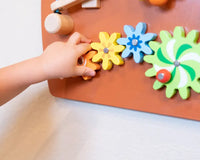 A small hand with light skin tone turns the cogs on the Horse Activity Wall Panel.