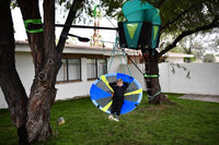 A child with light skin tone and short blonde hair lays back on the Slackers 50" Adventure Sky Swing as it moves backwards.