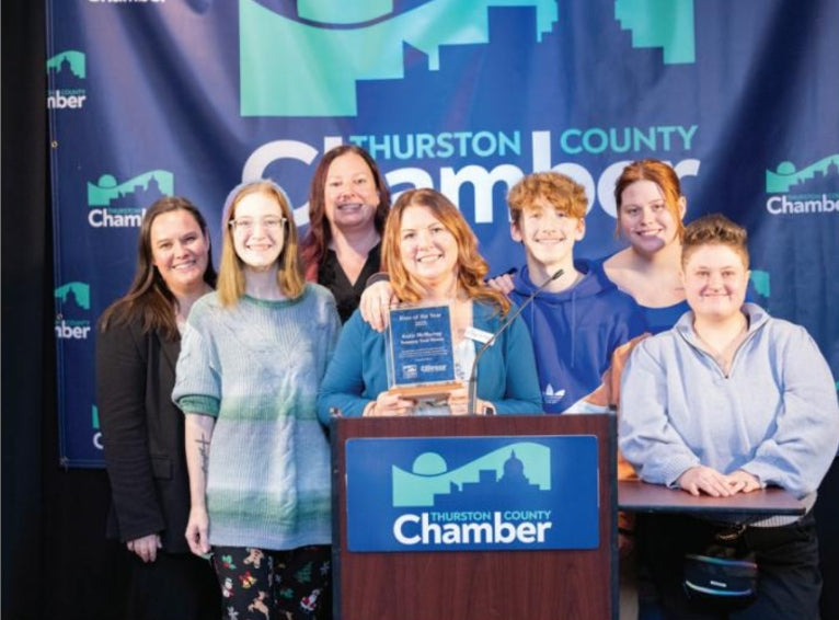 seven people smiling at the camera with one holding an award at a podium