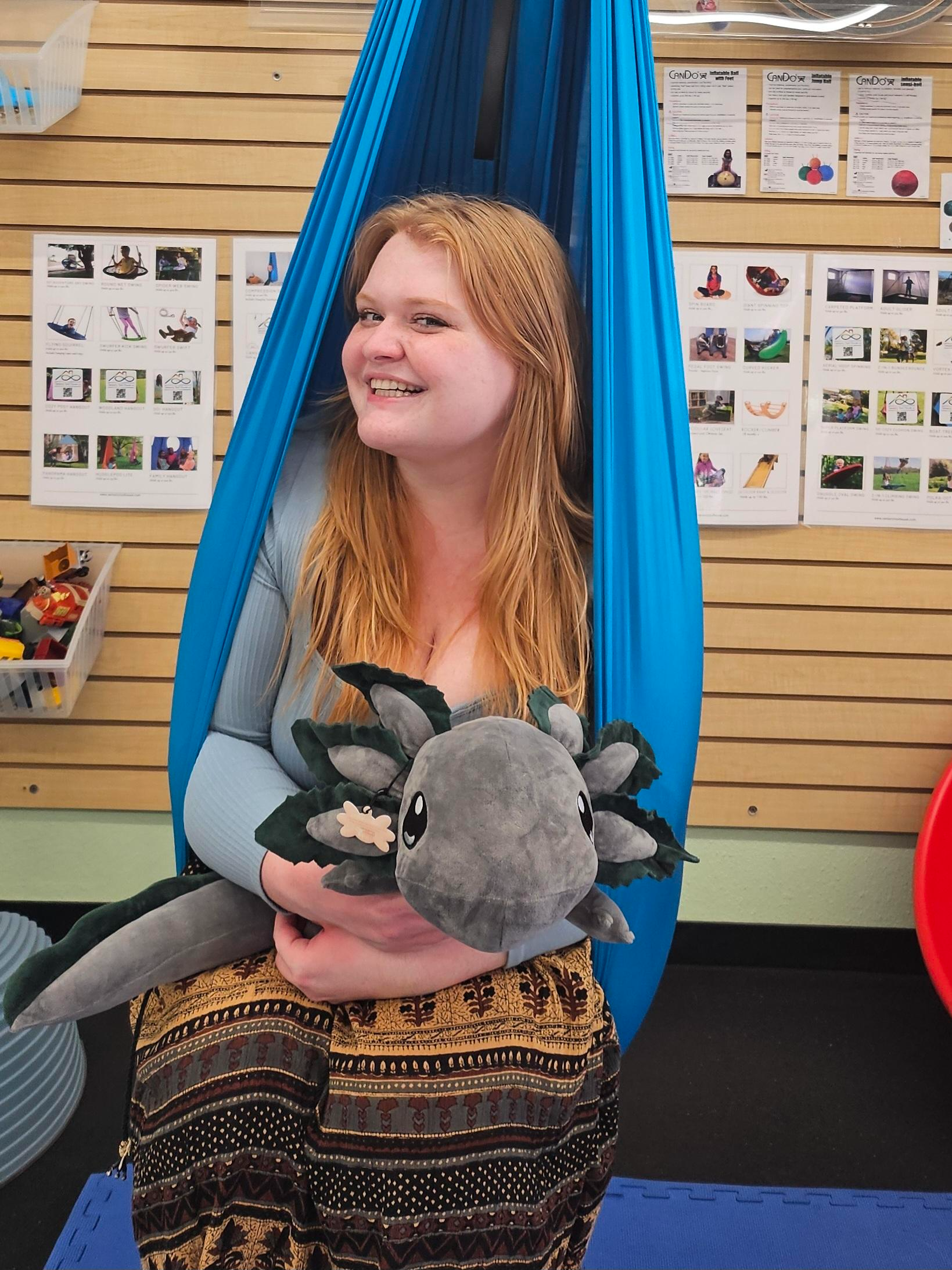 Woman smiling in a sensory swing holding a stuffed axolotl