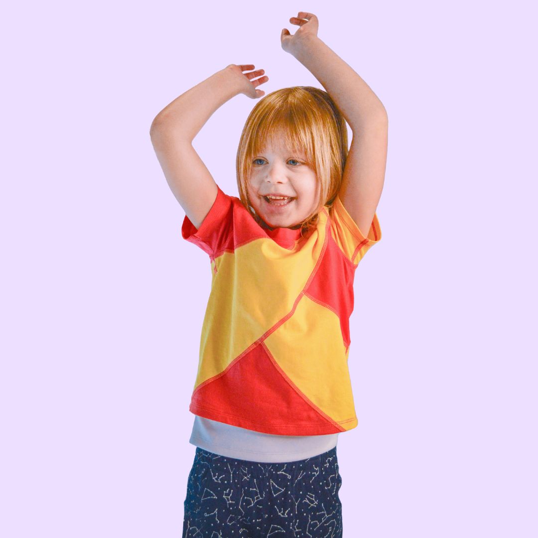 A child stands with their hands raised so that you can see the Coral-Yellow outer shirt and the bottom of the white compression undershirt.