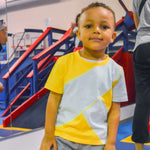 A child grins while wearing the Yellow and Mint Sensory Friendly T-Shirt at a gym.