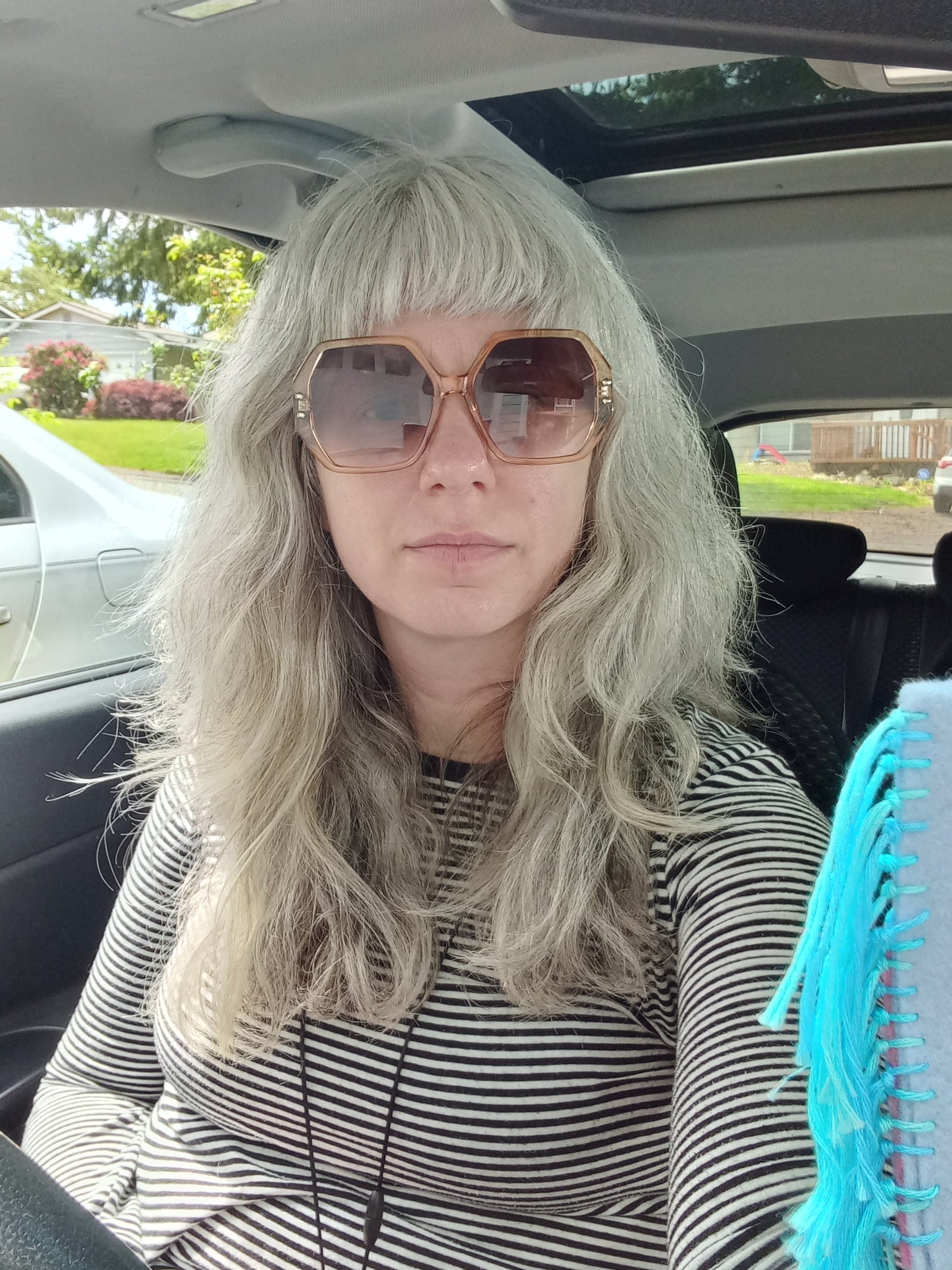 Person sitting in the car with long hair, and sunglasses on
