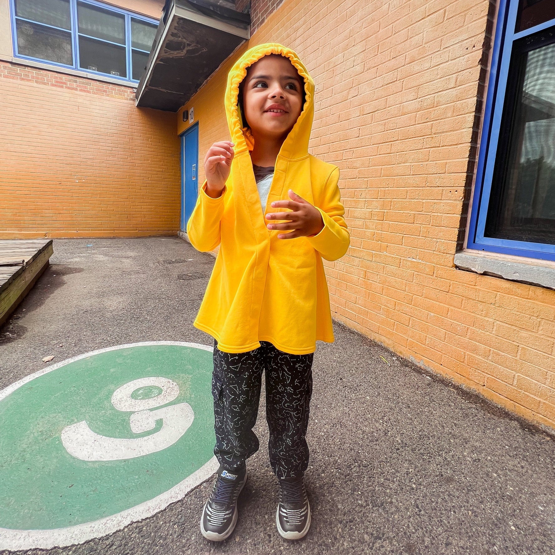 A child smiles while they wear the hood up on the yellow Sensory Friendly Hoodie.