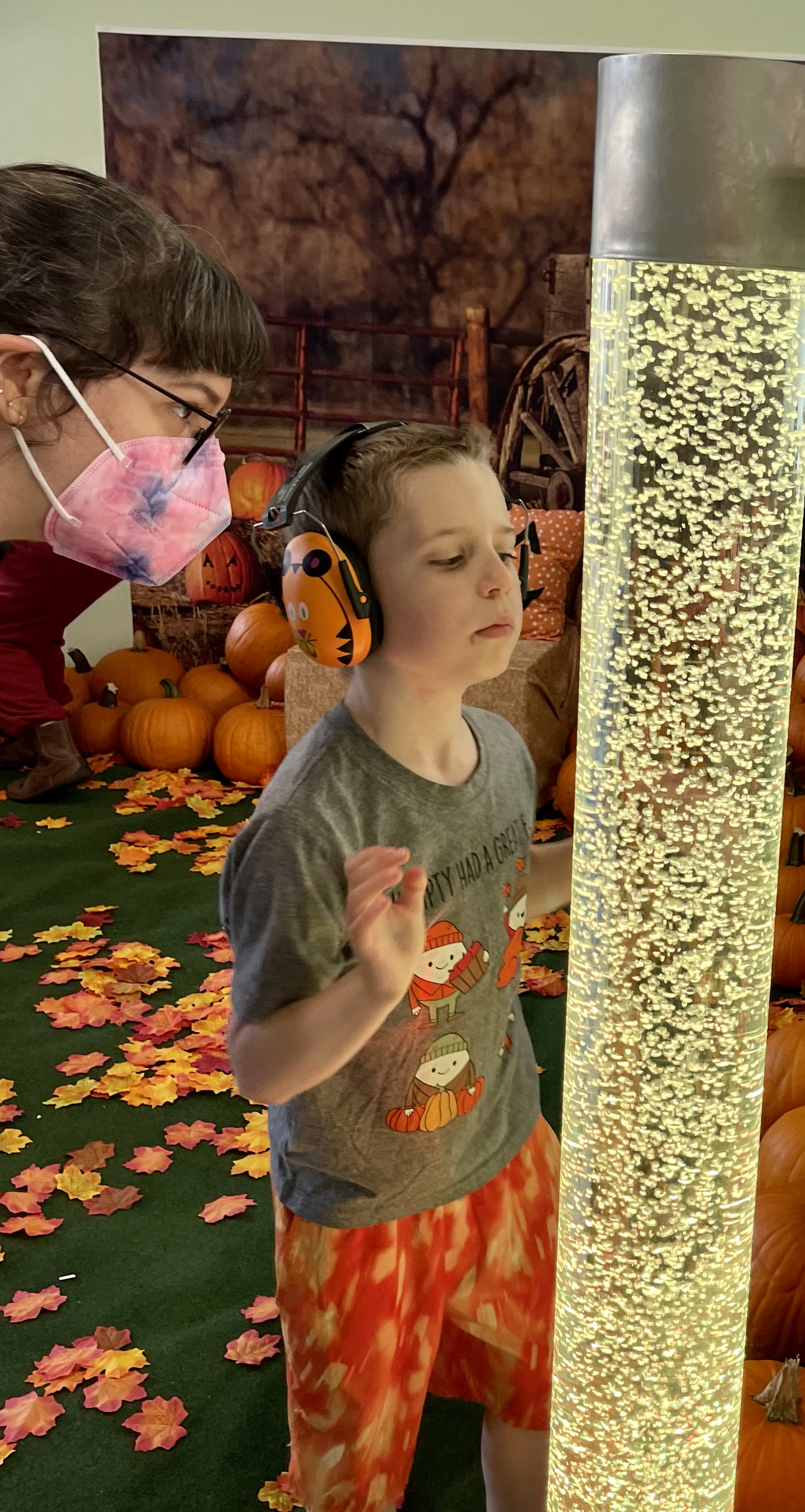 Young boy with noise reducing headphones looking at a bubble tube with an adult