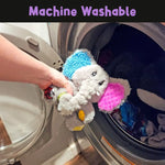 A hand puts The Mini Ellie Sensory Elephant Plush into the washer.