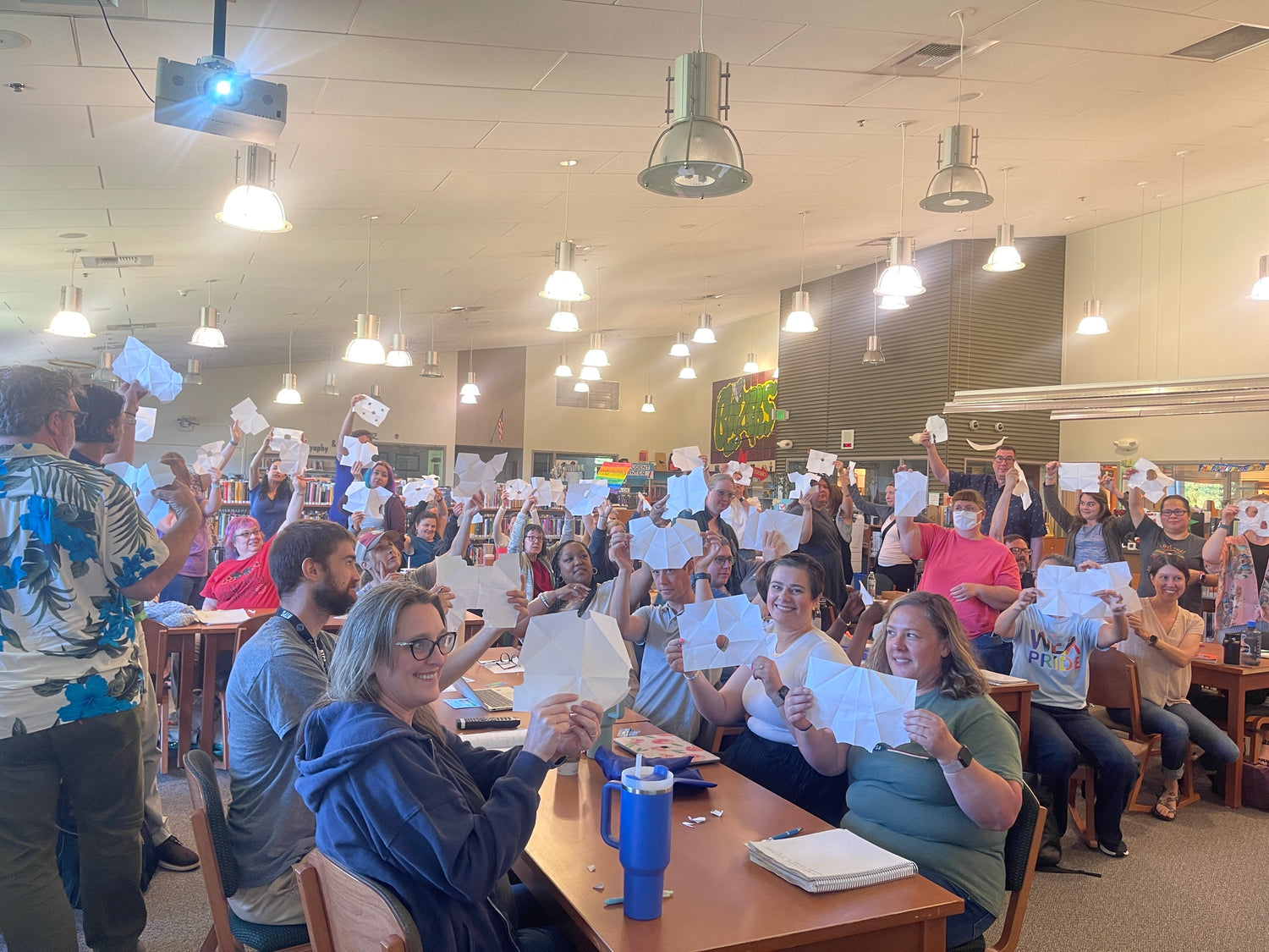 Large group in a library holding up torn paper