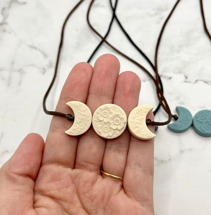 A hand with light skin tone holds up the Ivory Crescent Moon Phases Fidget Necklace.