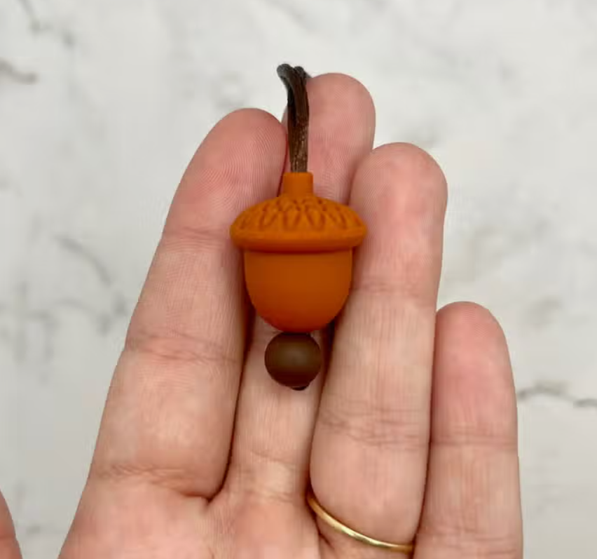 A hand with light skin tone is holding up the Acorn Fidget Necklace.