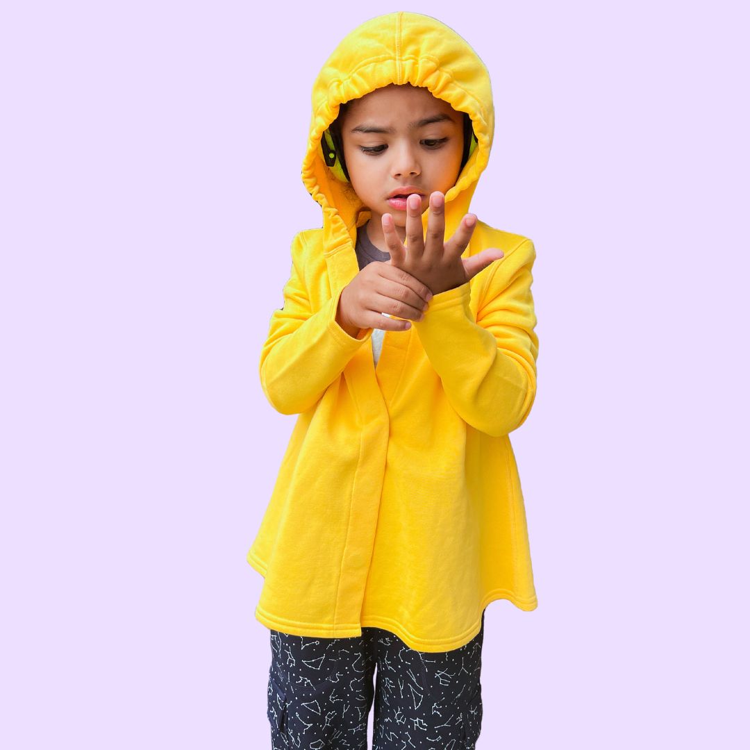 A child wears earmuffs under the hood of the yellow Sensory Friendly Hoodie.